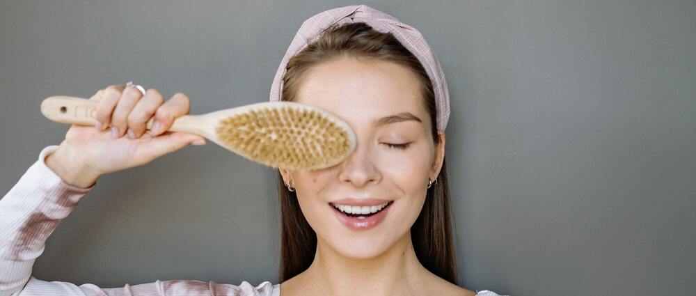 Moça alegre segurando uma escova de cabelo utilizada para seus cuidados capilares