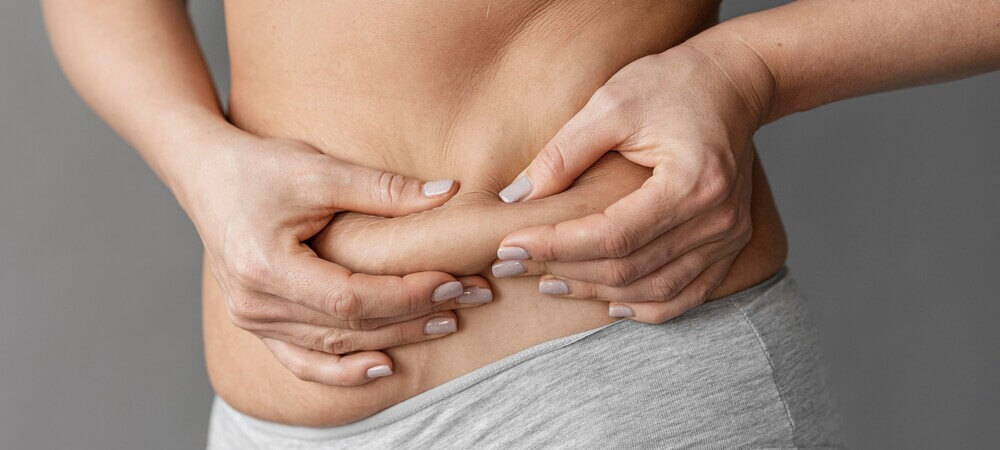 Mulher branca, com unhas de cor cinza, combinando com a roupa,apalpando seu excesso de gordura abdominal