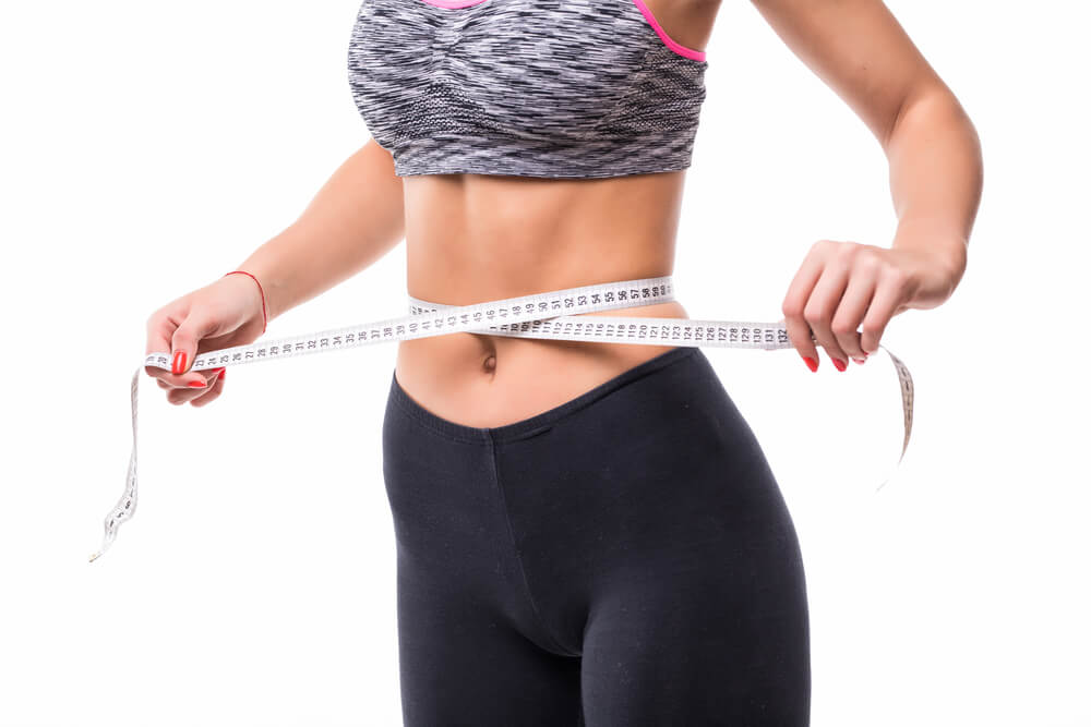Moça com roupa de ginástica medindo a circunferência abdominal