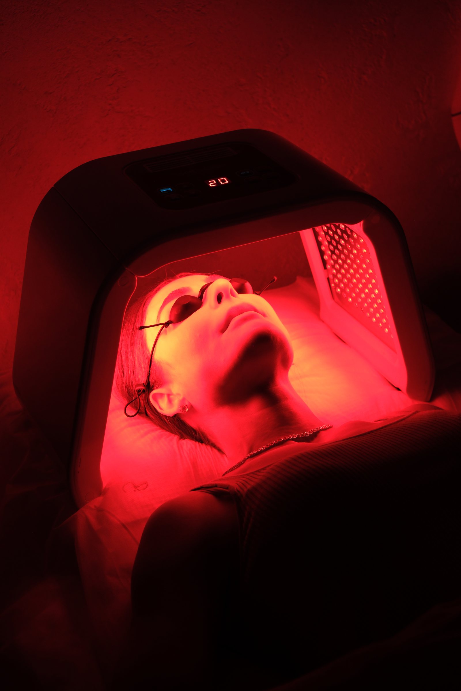 Pilar 3: Dermatologia Regenerativa — paciente recebendo terapia de LED vermelho no rosto, com óculos de proteção, sob o painel do aparelho