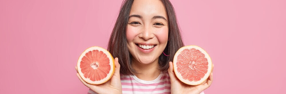 Garota sorridente segurando duas toranjas, que são alimentos bons para pele