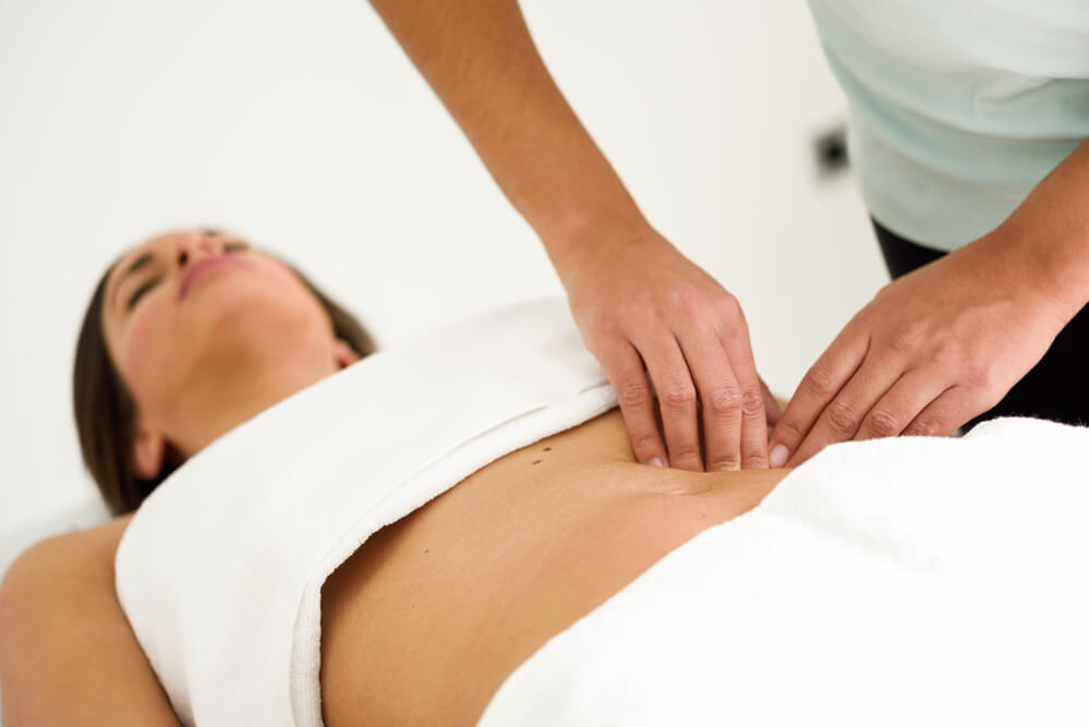 Profissional realizando massagem na barriga de paciente na técnica de drenagem pós operatória
